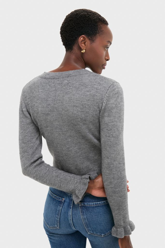 Person wearing Grey Knit Patterson Ruffle Sweater with ruffle cuffs and hem, paired with blue jeans, exudes an effortless and classic style.