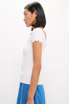 Young woman in a classic, effortless White Off-the-Shoulder Ric Rac Compression Elliston Shirt, showcasing high-end style with fun, scalloped sleeves and a sleek, modern look.