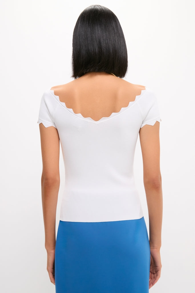 Model wearing the classic White Off-the-Shoulder Ric Rac Compression Elliston Shirt, showcasing its scalloped V-back neckline, paired with a bright blue skirt for an effortless, high-end look.