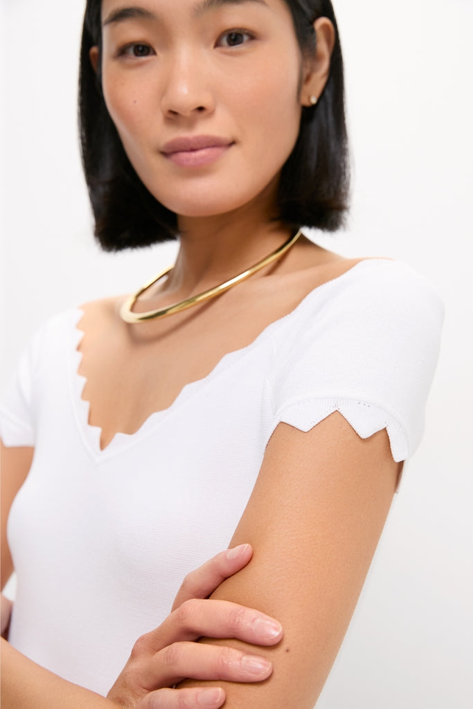 White Off-the-Shoulder Ric Rac Compression Elliston Shirt with scalloped neckline and sleeves, complemented by a classic gold necklace. Effortless, high-end style for fun, confident fashion.