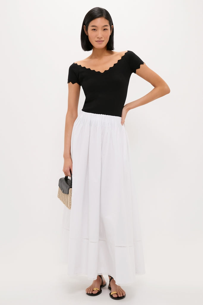 Young woman models the classic Black Off-the-Shoulder Ric Rac Compression Elliston Shirt, paired with an effortless maxi skirt and fun straw handbag for a high-end look.