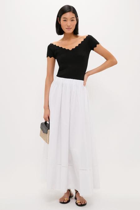 Young woman models the classic Black Off-the-Shoulder Ric Rac Compression Elliston Shirt, paired with an effortless maxi skirt and fun straw handbag for a high-end look.
