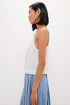 Woman in profile wearing the classic White Cotton Poplin Mandi Top, featuring thin straps, paired effortlessly with a high-waisted pleated skirt, embodying a fun, high-end style.