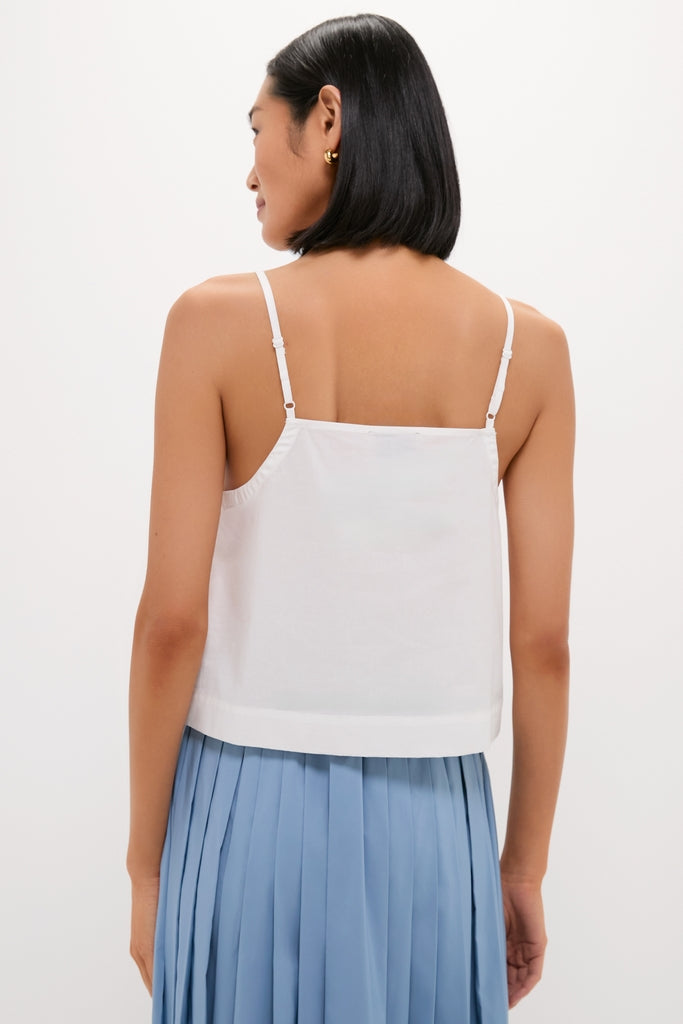 Person wearing the classic White Cotton Poplin Mandi Top with a spaghetti-strap design, paired with an effortless light blue pleated midi skirt, exuding a fun, high-end vibe.