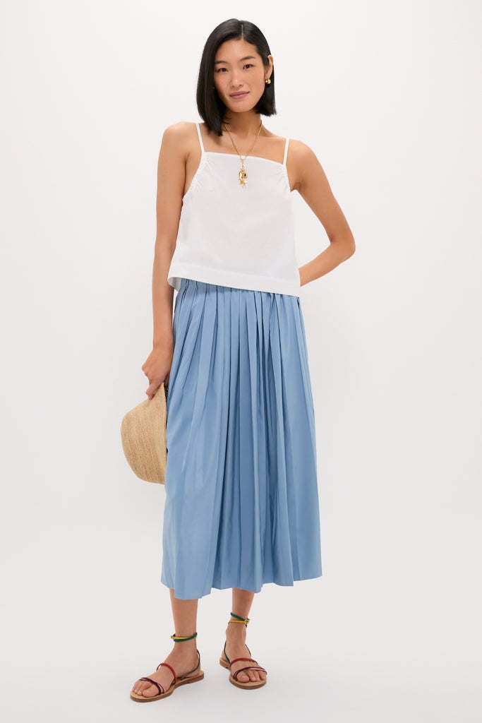 Slender woman models the classic White Cotton Poplin Mandi Top, paired with a pleated skirt, embodying effortless elegance and fun sophistication, perfect for a high-end, cool lifestyle.