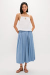 Young woman models the classic White Cotton Poplin Mandi Top, paired effortlessly with a pleated skirt and neutral sandals, exuding a high-end, fun style.