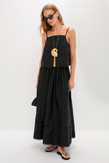 Woman in a classic, effortless Black Cotton Poplin Mandi Top and floor-length skirt, accessorized with a woven handbag, sculptural necklace, and cat-eye sunglasses.