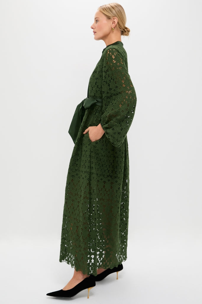 A woman models the classic Forest Green Lace Calliope Dress with puffed sleeves, satin sash, and pockets, embodying an effortless, high-end style.