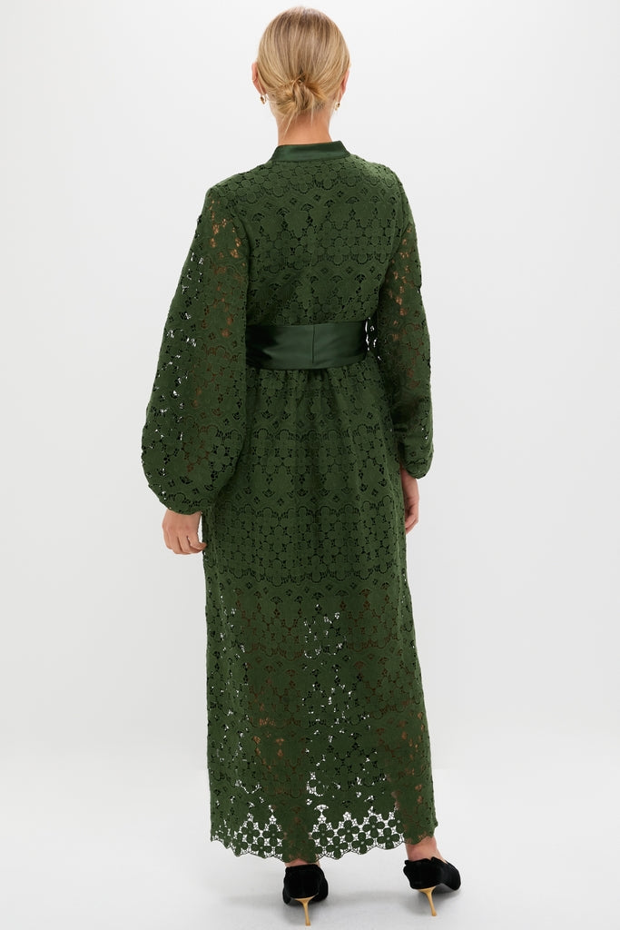 Woman in a classic, floor-length Forest Green Lace Calliope Dress with puffed sleeves and satin sash, embodies effortless elegance and high-end style.