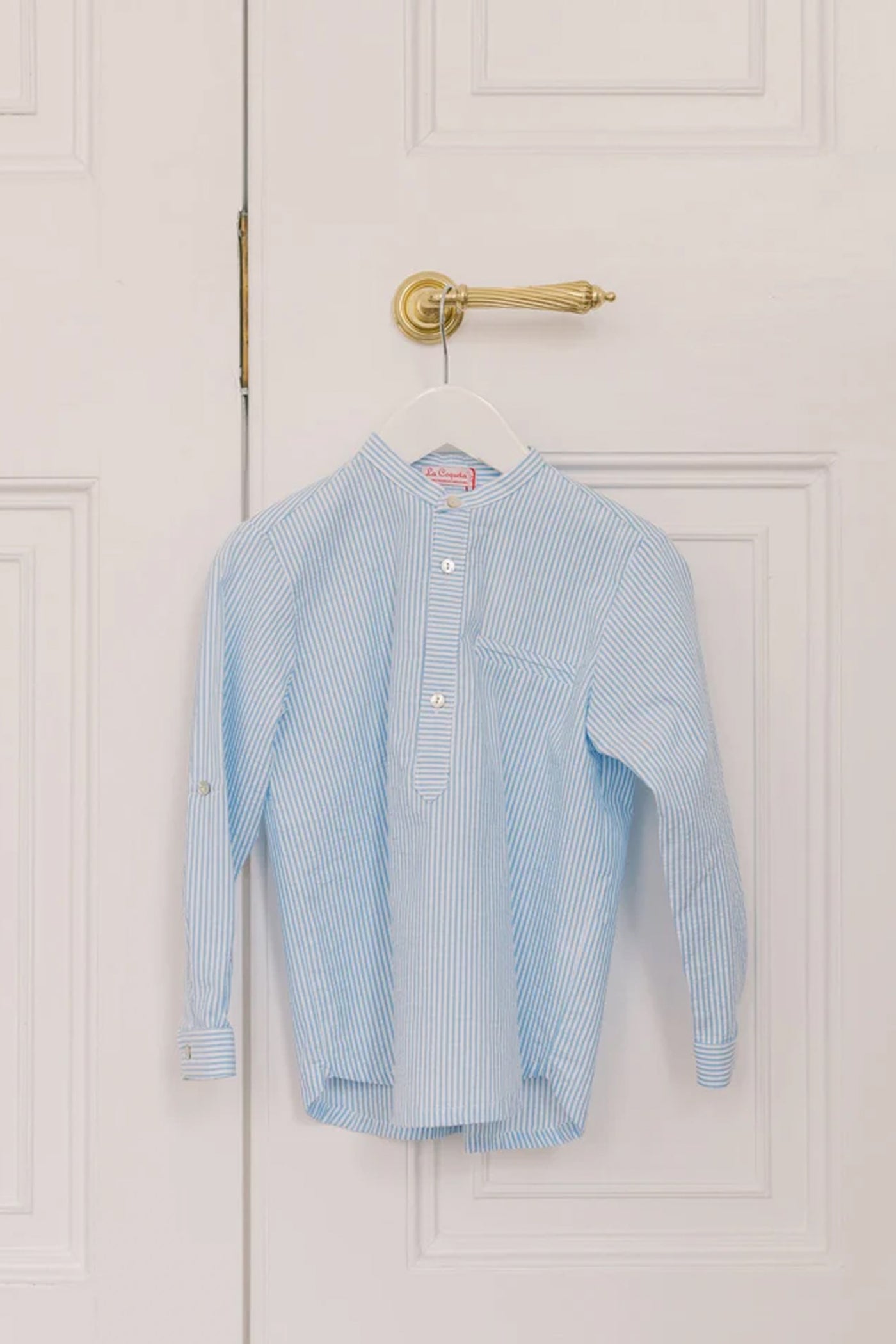Blue Stripe Mateo Long Sleeve Shirt with mandarin collar and chest pocket, hanging on a door. Classic and effortless high-end style for fun and smart-casual occasions.