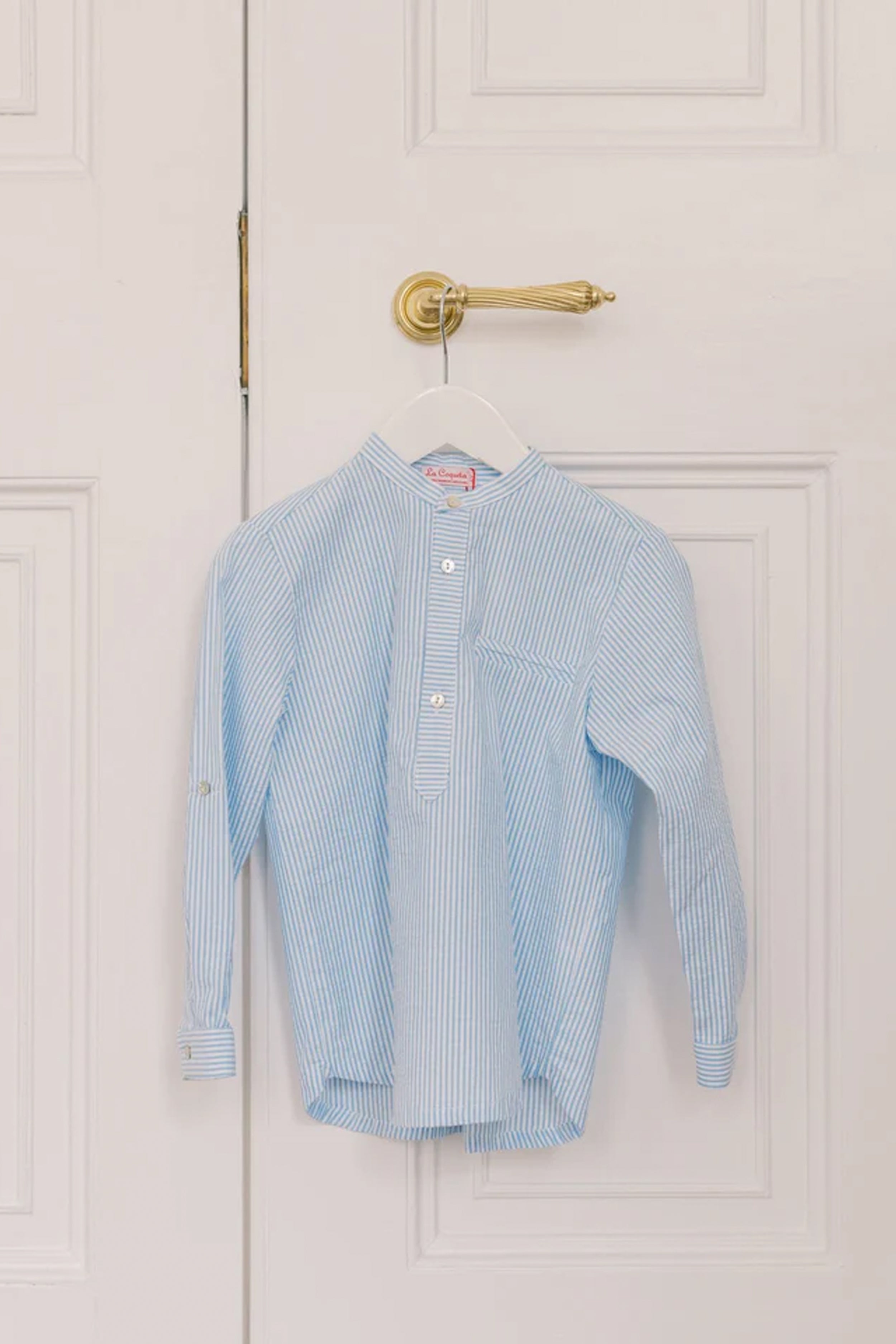 Blue Stripe Mateo Long Sleeve Shirt with mandarin collar and chest pocket, hanging on a door. Classic and effortless high-end style for fun and smart-casual occasions.