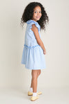 Young girl in profile wearing the Blue Gingham Fabiola Drop Waist Dress with butterfly sleeves, embodying classic, effortless style. Perfect for fun, everyday moments and high-end occasions.