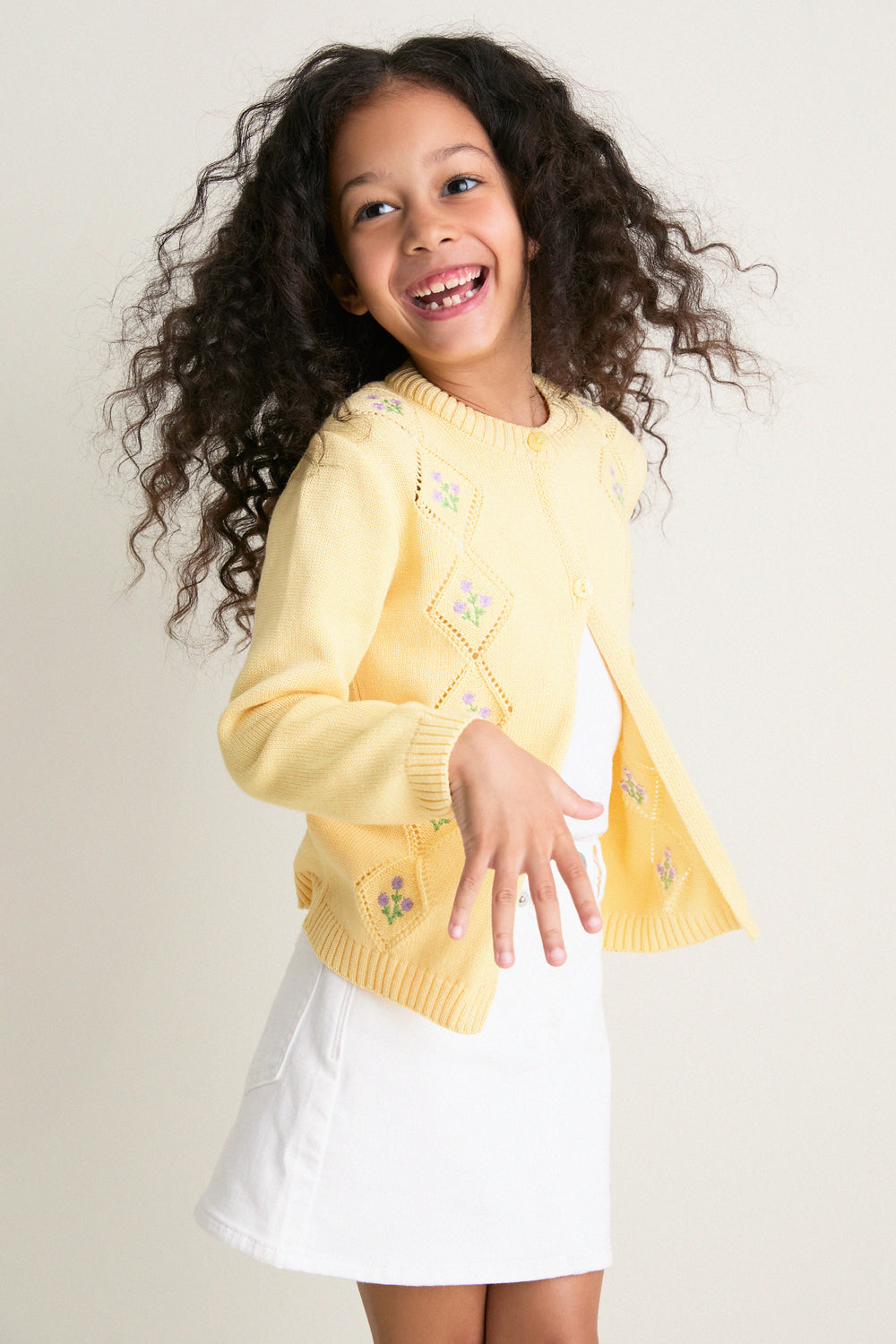 Young girl in mid-motion, wearing the Lemon Espina Cotton Cardigan. The classic, high-end design features effortless pointelle details and fun floral embroidery, perfect for any occasion.