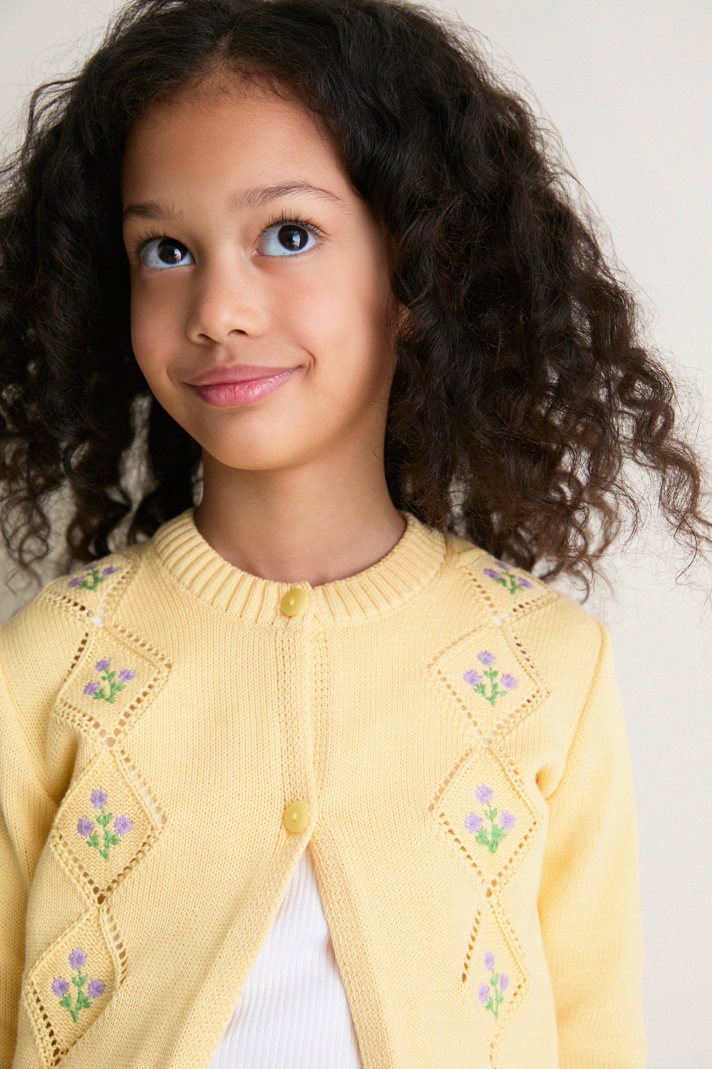 Young girl wearing the Lemon Espina Cotton Cardigan, showcasing its classic, effortless design with fun floral embroidery and high-end mother of pearl buttons.