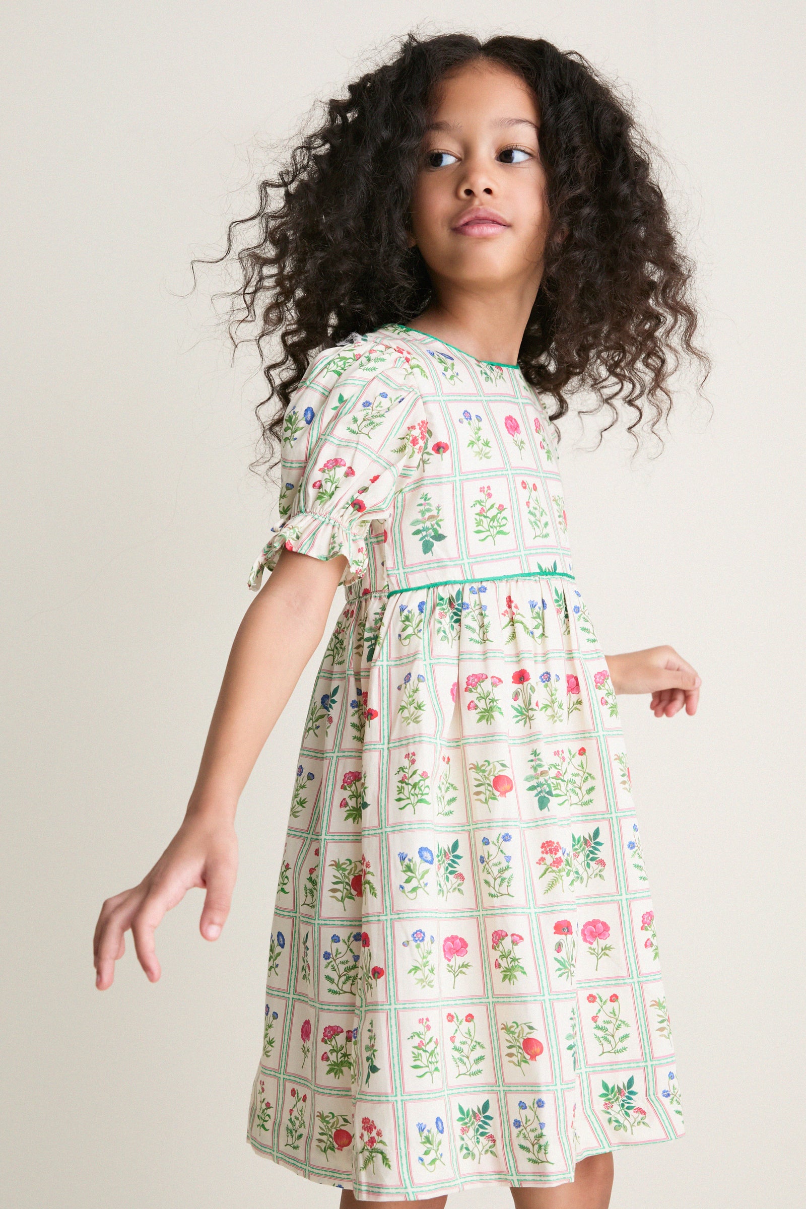 Young girl in a classic, high-end Ivory Botanical Olivia Dress with floral grid design, embodying effortless, fun elegance from Tuckernuck.