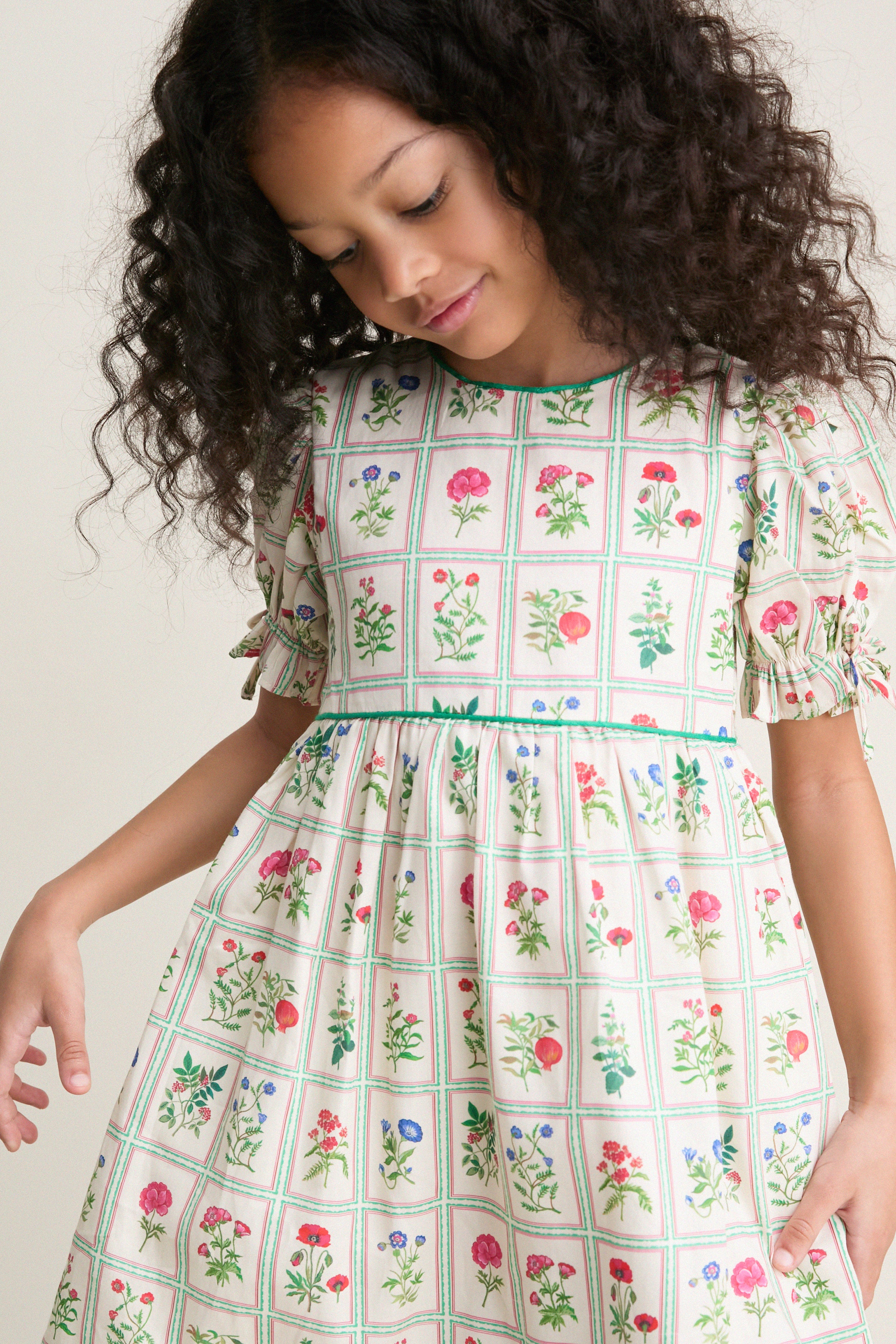 Young girl in a classic, high-waisted Ivory Botanical Olivia Dress with puff sleeves and a flared skirt, featuring an effortless, fun botanical print for high-end charm.