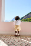 Child in classic Yellow Gingham Oliver Baby Boy Set, featuring a Peter Pan collar and elastic waist, gazes at scenic view, embodying effortless, high-end style for warm-weather fun.