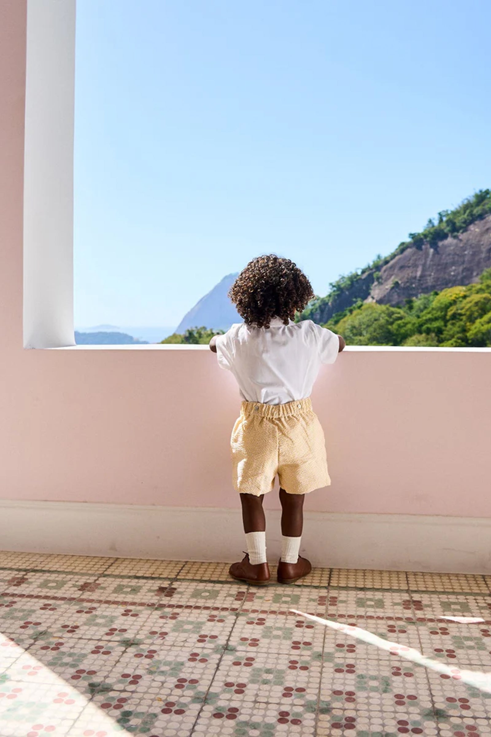 Child in classic Yellow Gingham Oliver Baby Boy Set, featuring a Peter Pan collar and elastic waist, gazes at scenic view, embodying effortless, high-end style for warm-weather fun.