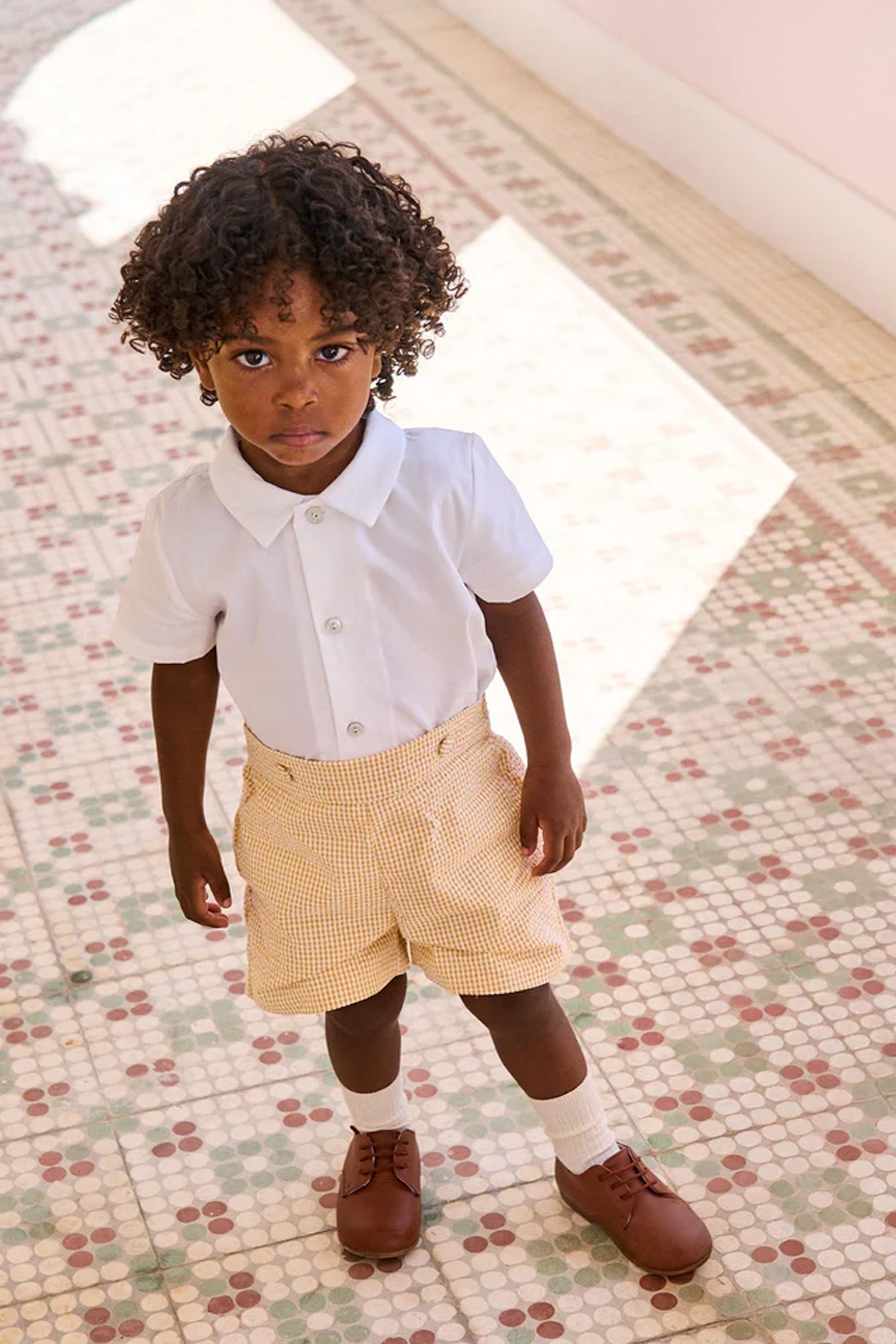 Young child in the classic Yellow Gingham Oliver Baby Boy Set, featuring an effortless, high-end white shirt and fun gingham shorts, embodying playful sophistication.