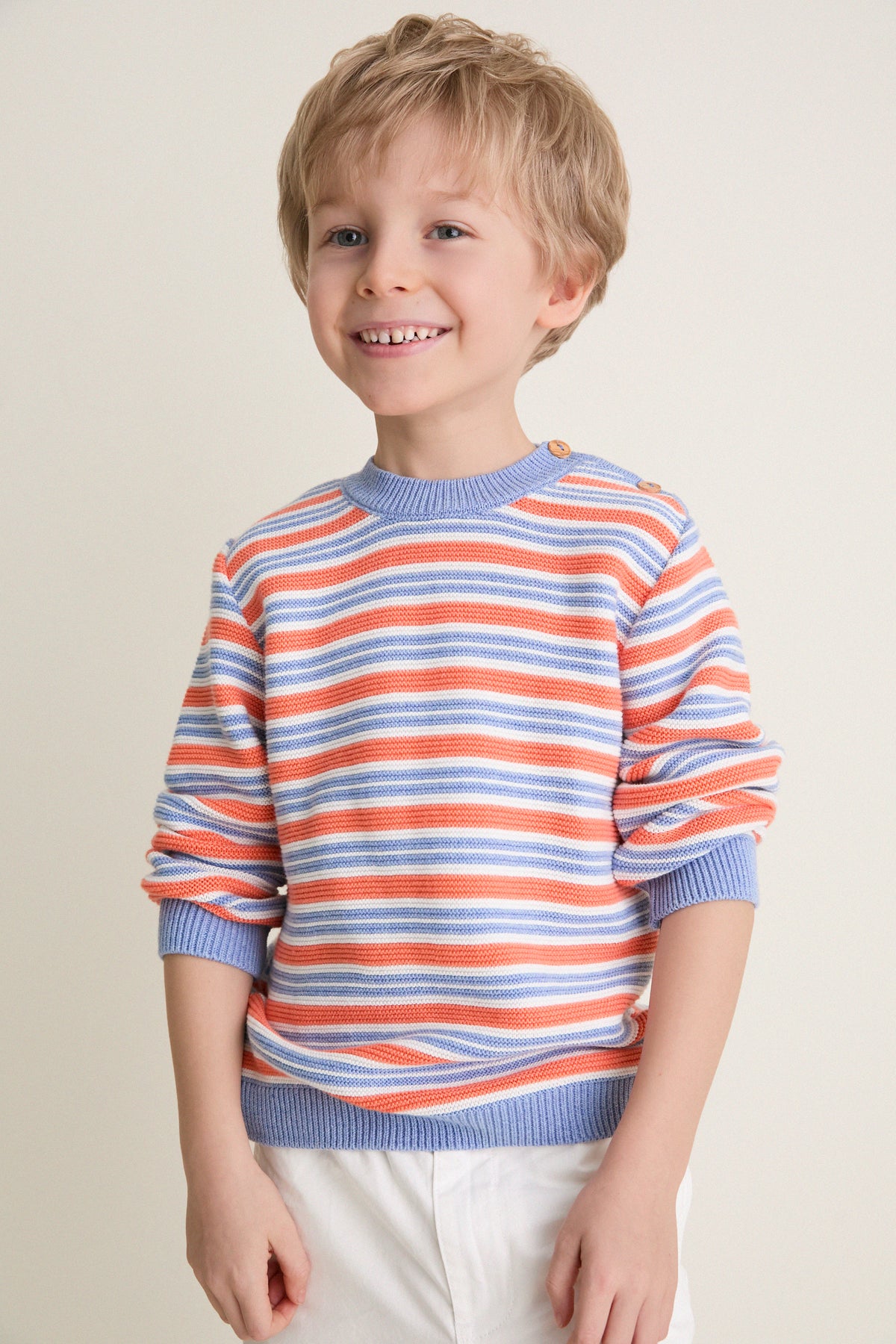 Young boy wearing the classic Coral Stripe Bromo Cotton Jumper, featuring intarsia stripes, ribbed trims, and wooden buttons, embodying effortless, high-end style.