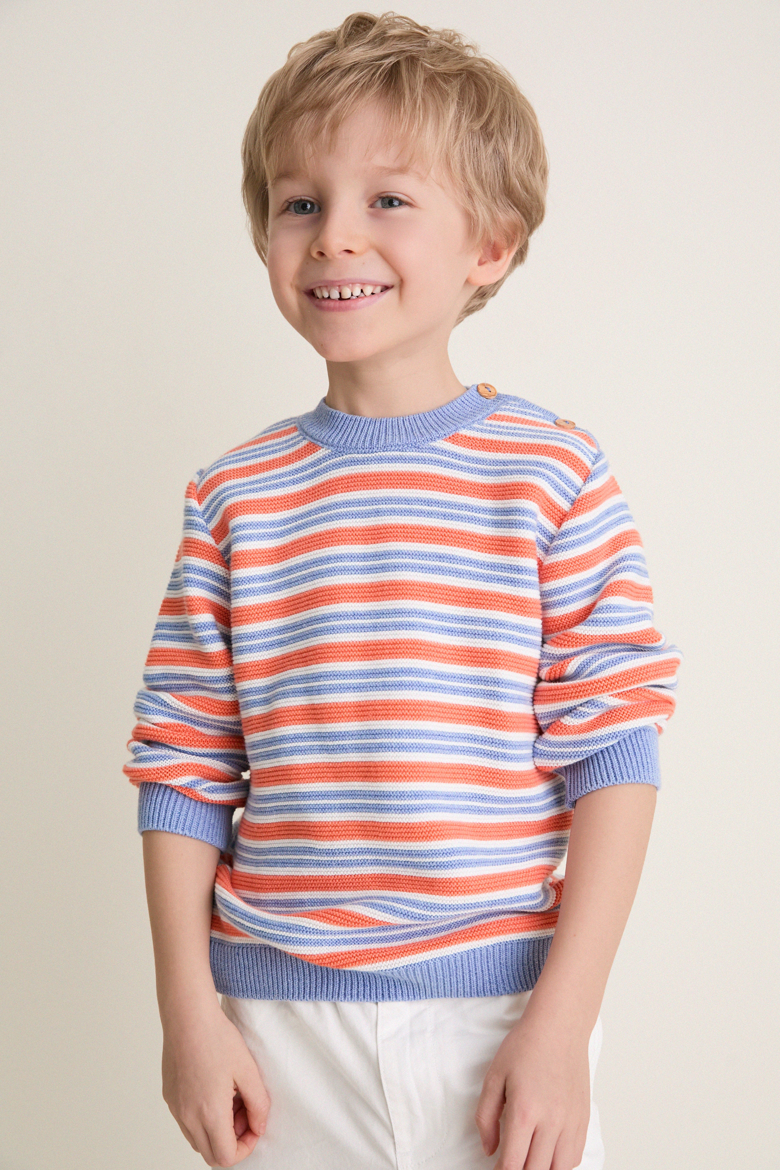Young boy wearing the classic Coral Stripe Bromo Cotton Jumper, featuring intarsia stripes, ribbed trims, and wooden buttons, embodying effortless, high-end style.
