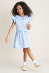 Young girl in a gingham dress wearing Pale Yellow Leather T-Bar Shoes, embodying classic, effortless style with high-end craftsmanship and fun, adjustable buckle straps.