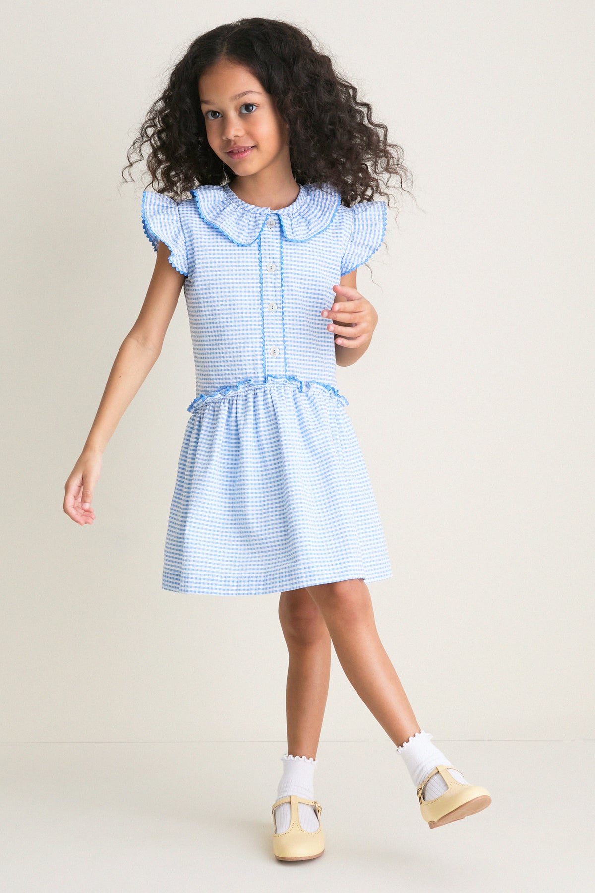 Young girl in a gingham dress wearing Pale Yellow Leather T-Bar Shoes, embodying classic, effortless style with high-end craftsmanship and fun, adjustable buckle straps.