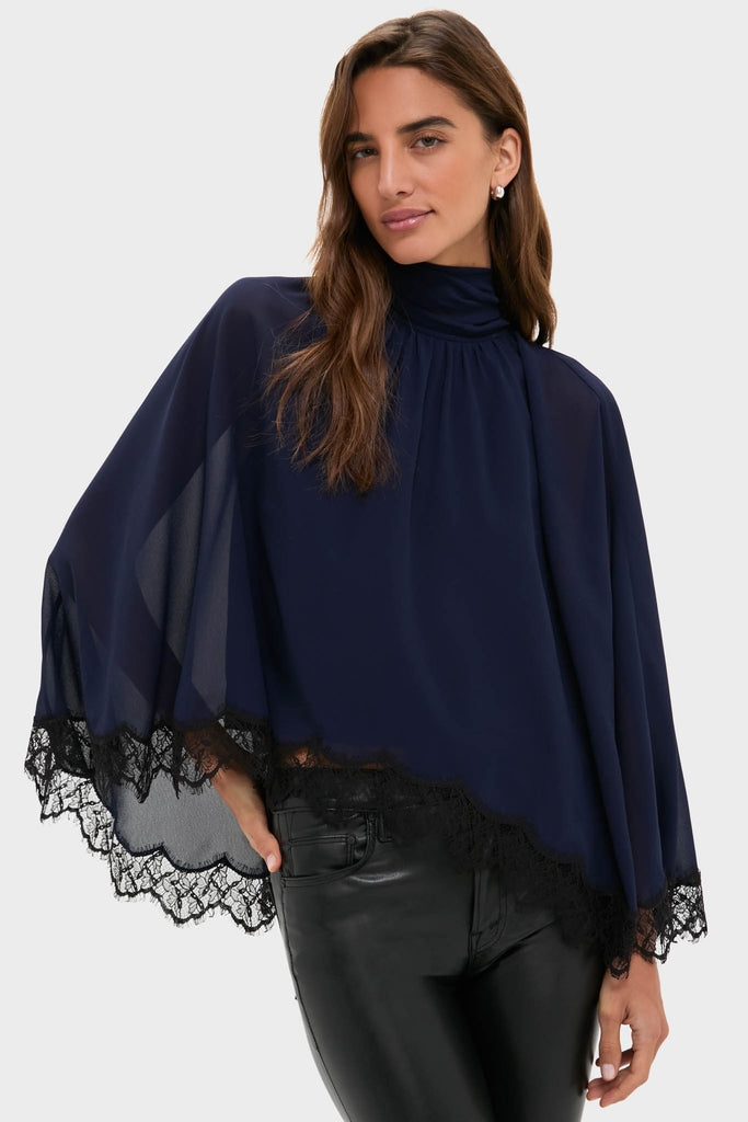 Model wearing the classic Navy Cape Chiffon Ashfield Top with mock neck and lace-trimmed cape, paired effortlessly with sleek black pants for a high-end, fun look.