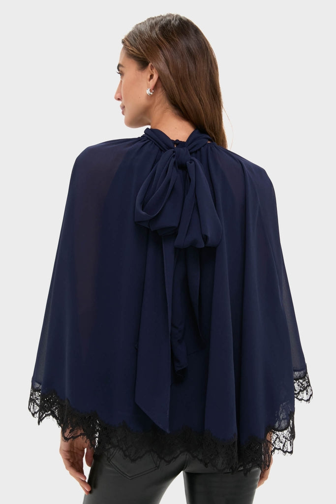 Navy Cape Chiffon Ashfield Top: A classic, effortless, high-end chiffon cape with lace trim, mock neck, and bow detail, perfect for fun, elevated occasions.