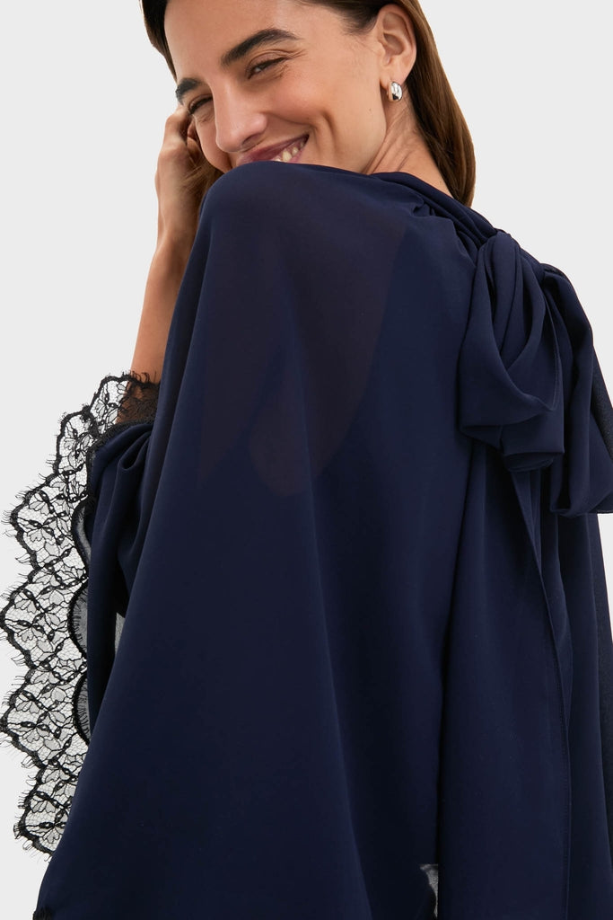 Woman smiling in a classic, effortless Navy Cape Chiffon Ashfield Top with a chic mock neck and elegant lace-trimmed sleeves, embodying high-end, fun style.