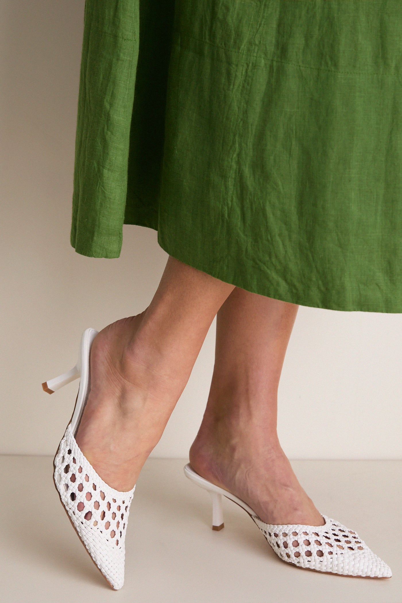 White Tia Heels on display, featuring a classic, woven mule design with pointed toes and a low stiletto heel, embodying effortless, high-end style for versatile, fun occasions.
