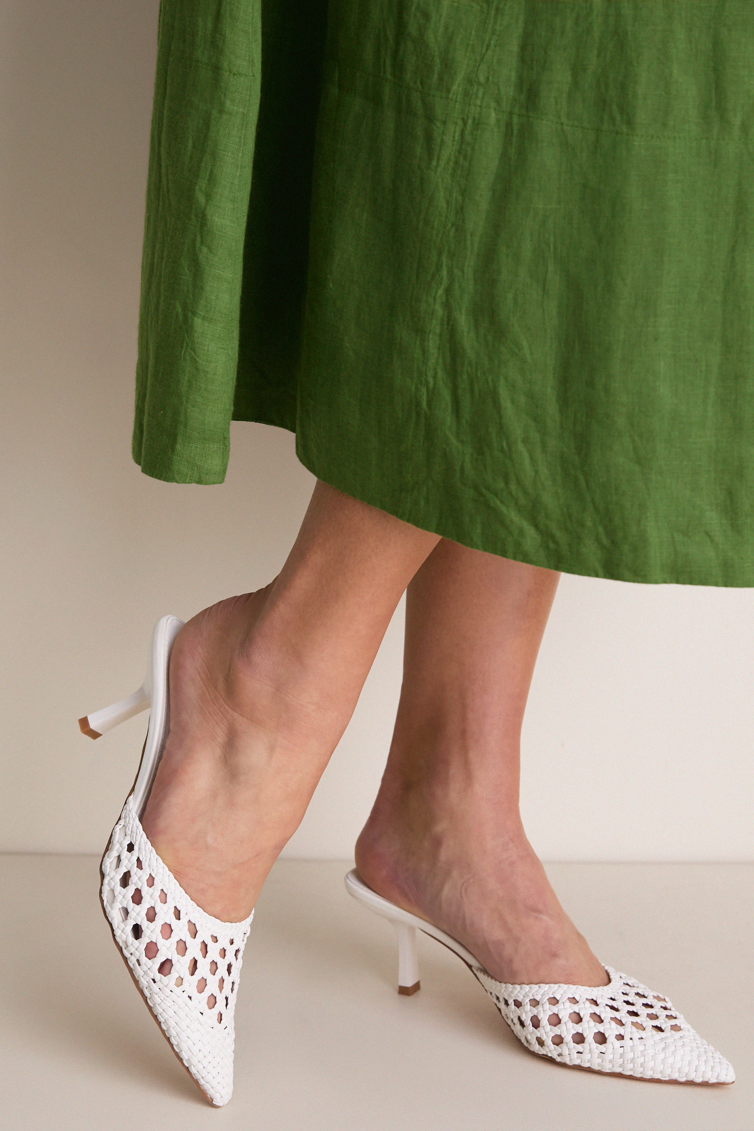 White Tia Heels on display, featuring a classic, woven mule design with pointed toes and a low stiletto heel, embodying effortless, high-end style for versatile, fun occasions.