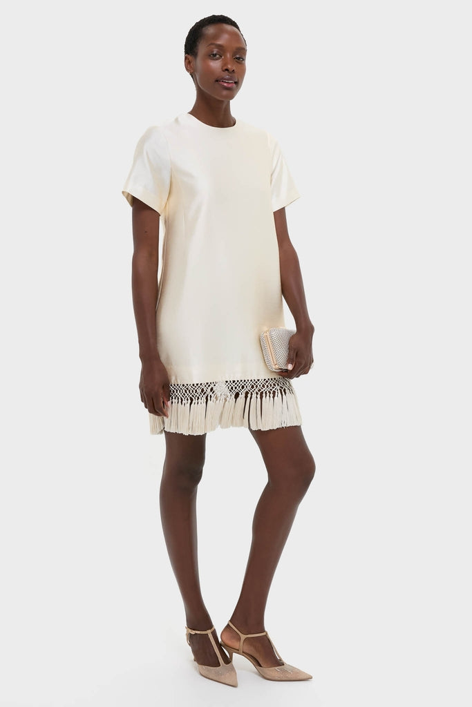 Model in the Winter White Tassel Dupioni Downing Dress, showcasing a classic, high-end shift style with effortless macramé fringe. Paired with a metallic clutch and fun T-strap heels.