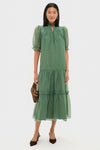 Woman in a classic, sage-green chiffon Selena Maxi Dress with a high collar, puff sleeves, and tiered skirt, paired with a leopard-print handbag and brown slingback heels.