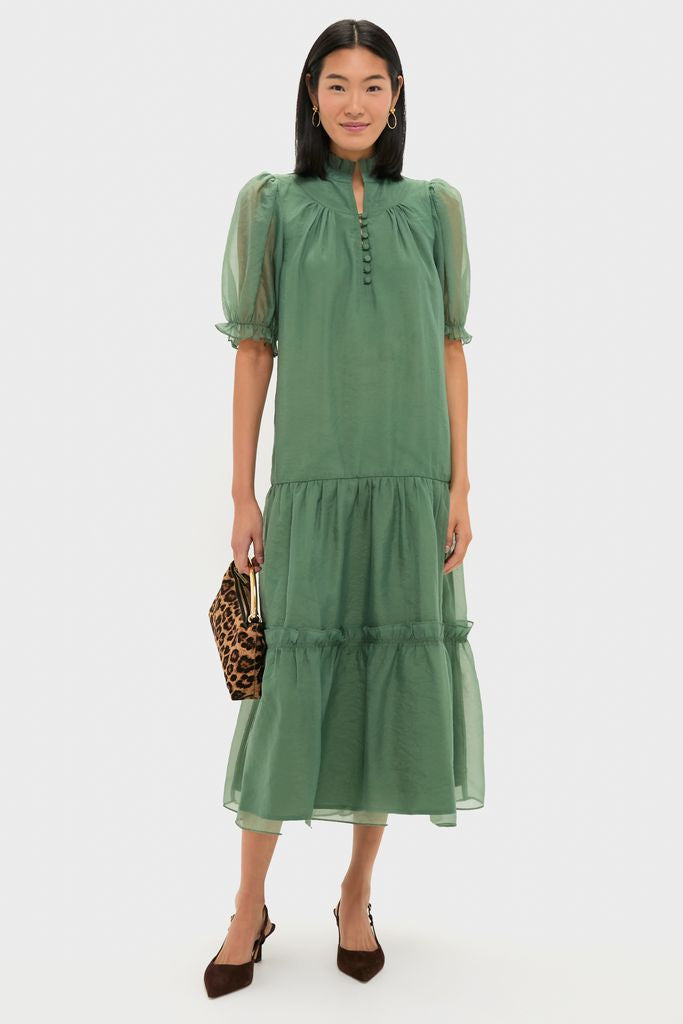 Woman in a classic, sage-green chiffon Selena Maxi Dress with a high collar, puff sleeves, and tiered skirt, paired with a leopard-print handbag and brown slingback heels.