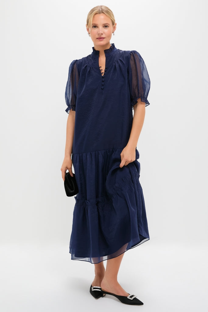 Woman models the Navy Chiffon Selena Maxi Dress, featuring a classic ruffled collar, sheer puff sleeves, and a tiered skirt. Effortless and high-end, perfect for fun occasions.