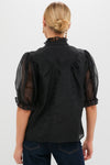 Back view of a classic Black Chiffon Selena Blouse with sheer puff sleeves and ruffled collar, paired with a low bun and dangling earrings, exuding effortless, high-end style.