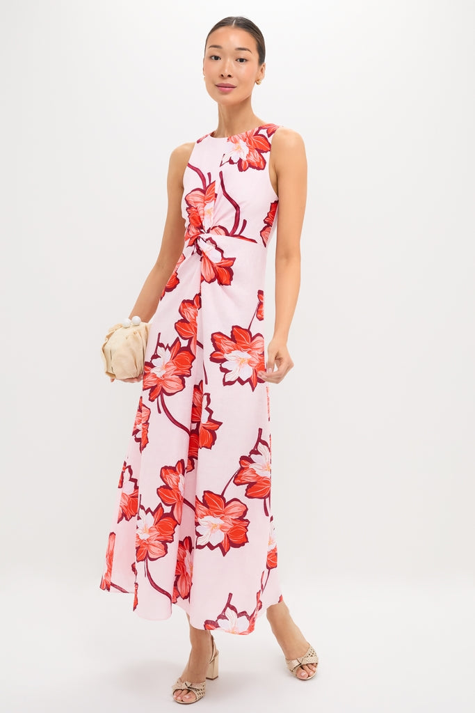 Woman in Lani Maxi Dress with vibrant floral print and knotted waist detail, holding a beige clutch, embodying classic, effortless style with a fun, high-end appeal.