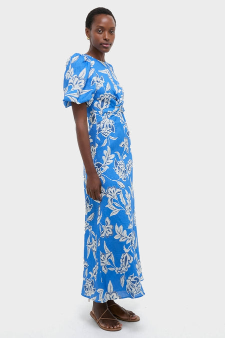Ren Cut Out Maxi Dress: A classic and effortless cobalt-blue dress with a floral pattern, featuring puffed sleeves and a flowing skirt, paired with fun, high-end sandals.