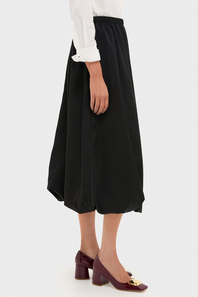 Woman wearing the Black Clairmont Bubble Skirt, featuring a voluminous silhouette and elastic waistband, paired with glossy burgundy block-heel pumps for a classic, effortless look.