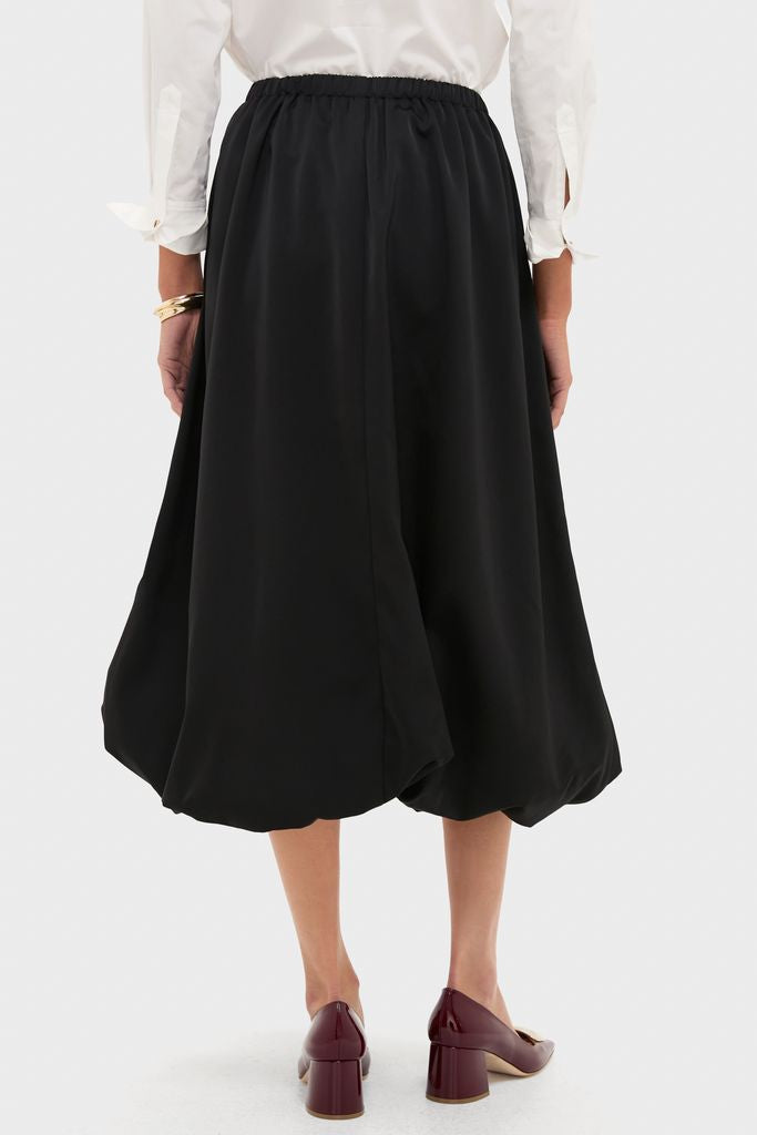 Woman wearing classic Black Clairmont Bubble Skirt, showcasing its effortless style with an elastic waistband, paired with a white blouse and burgundy block-heel pumps.