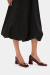 Black Clairmont Bubble Skirt paired with burgundy patent-leather pumps featuring gold accents, offering a classic, effortless, and high-end style. Perfect for a fun, confident look.