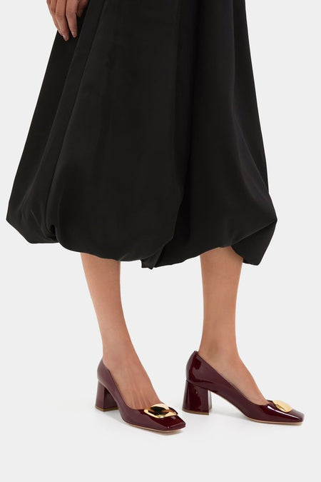 Black Clairmont Bubble Skirt paired with burgundy patent-leather pumps featuring gold accents, offering a classic, effortless, and high-end style. Perfect for a fun, confident look.