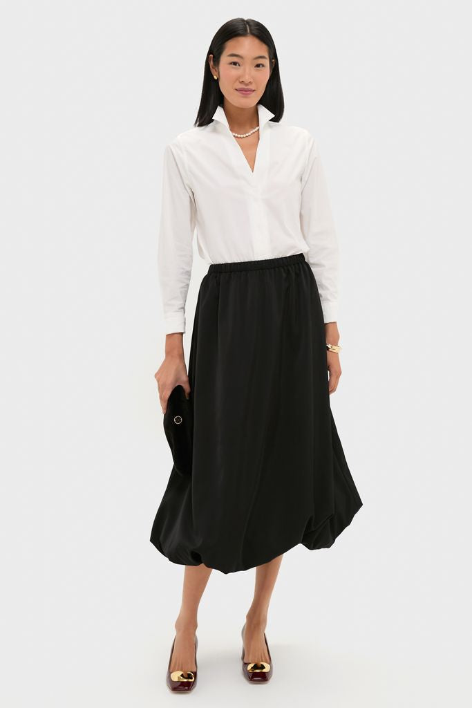 Woman wearing Black Clairmont Bubble Skirt paired with a white blouse, accessorized with a small black clutch, pearl necklace, and burgundy heels for an effortless, high-end look.