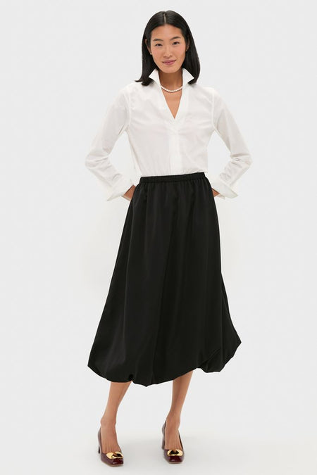 Woman in a classic, high-end Black Clairmont Bubble Skirt, styled effortlessly with a white blouse and burgundy pumps, exuding fun and confidence.