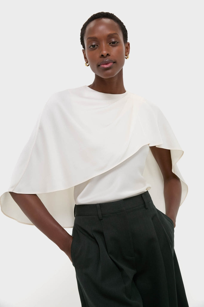 Cream Eliora Cape Top: Classic asymmetric drape, effortless elegance with a relaxed fit. Paired with tailored trousers, embodying high-end, fun, modern sophistication.