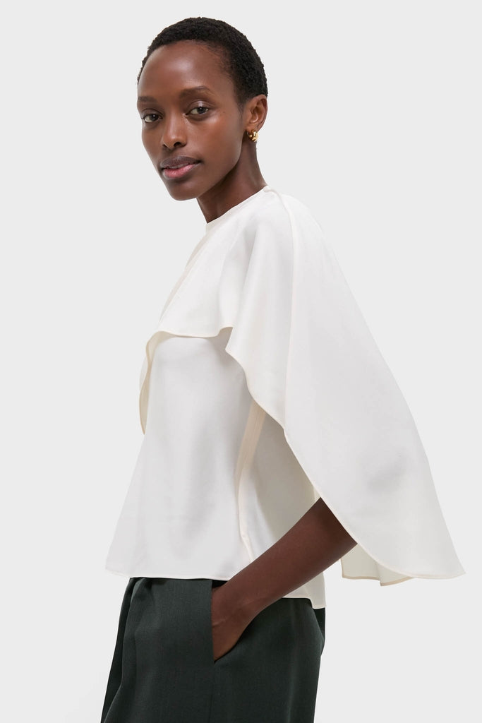 Cream Eliora Cape Top on model, showcasing classic, effortless elegance with asymmetric draped overlay and relaxed fit, embodying high-end, fun style.