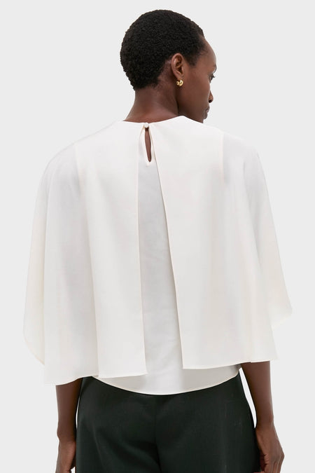 Model in Cream Eliora Cape Top showcasing classic, effortless style with asymmetric satin overlay, keyhole detail, paired with tailored trousers, embodying high-end, fun, modern elegance.