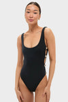 Woman in Black Mona Scoop Neck One Piece, featuring silver-tone hardware and cheeky coverage, embodies a classic, high-end, effortless style with playful cut-out sides.