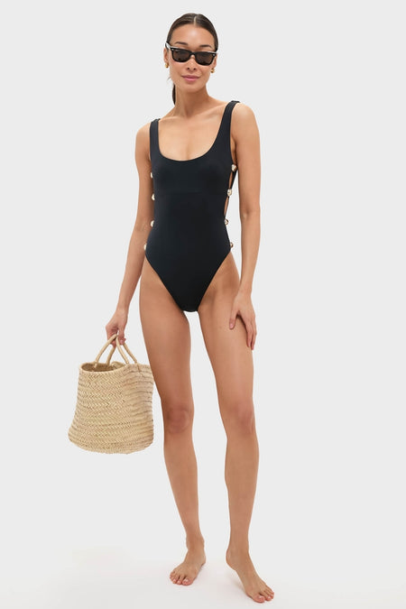 Model wearing Black Mona Scoop Neck One Piece with silver-tone side hardware, holding a straw tote and wearing sunglasses, exuding classic, effortless, and high-end style.
